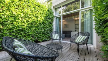 A wooden deck with wicker furniture and a green hedge.