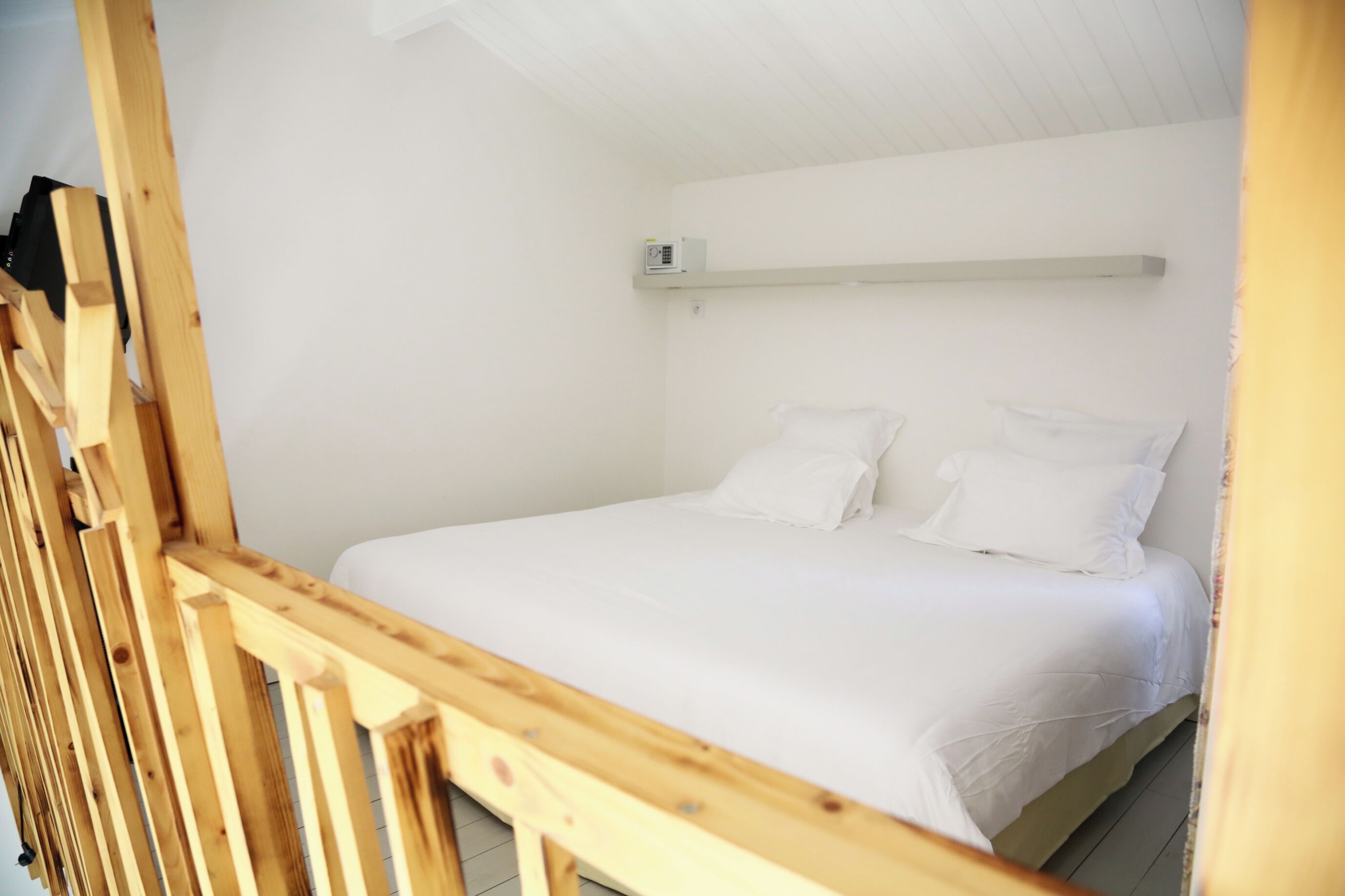 A single bed with white bedding in a room with white walls and a wooden headboard.