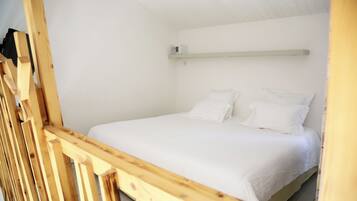 A single bed with white bedding in a room with white walls and a wooden headboard.