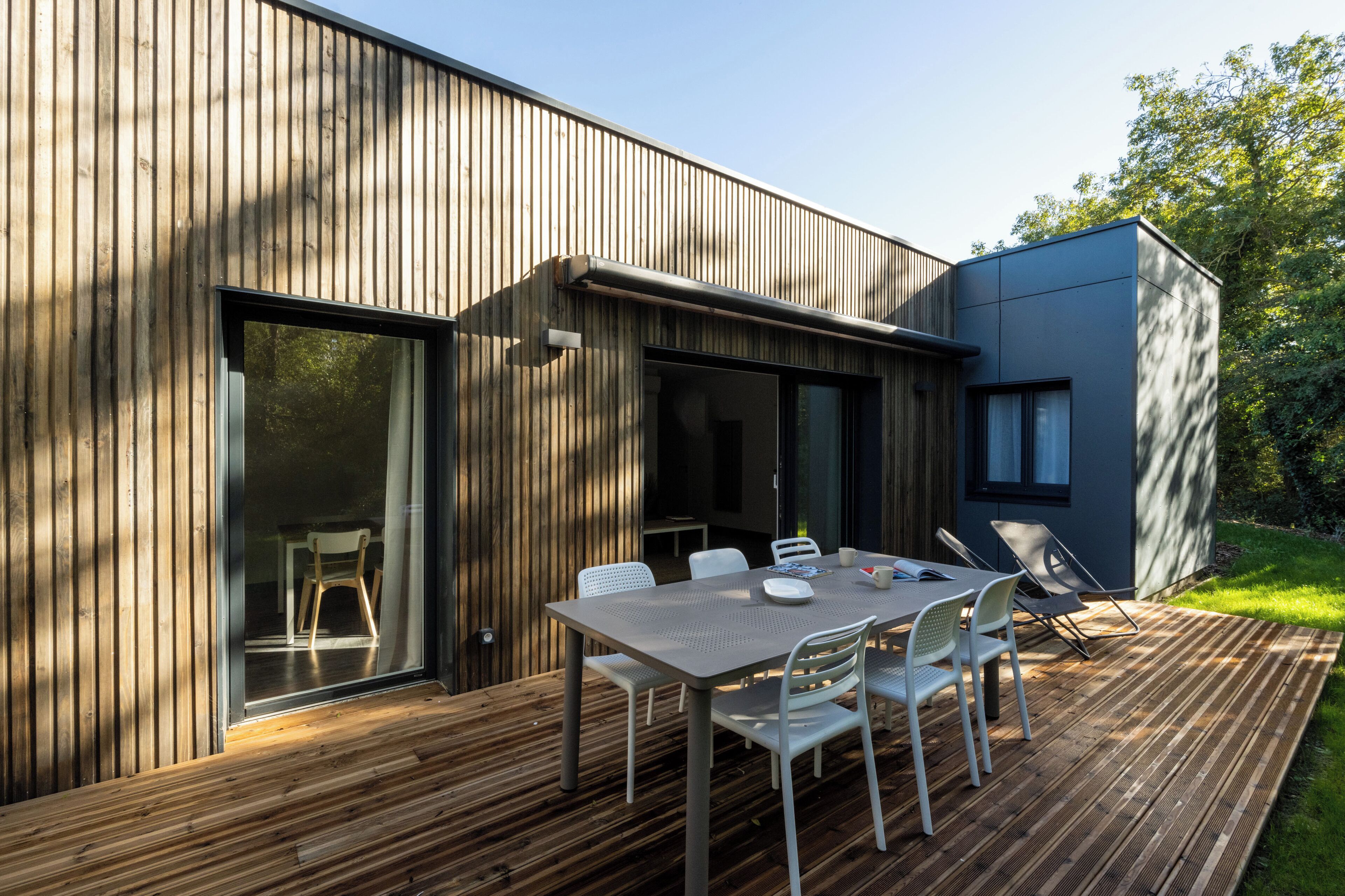A modern outdoor dining area with a wooden deck, a metal table, and white chairs.