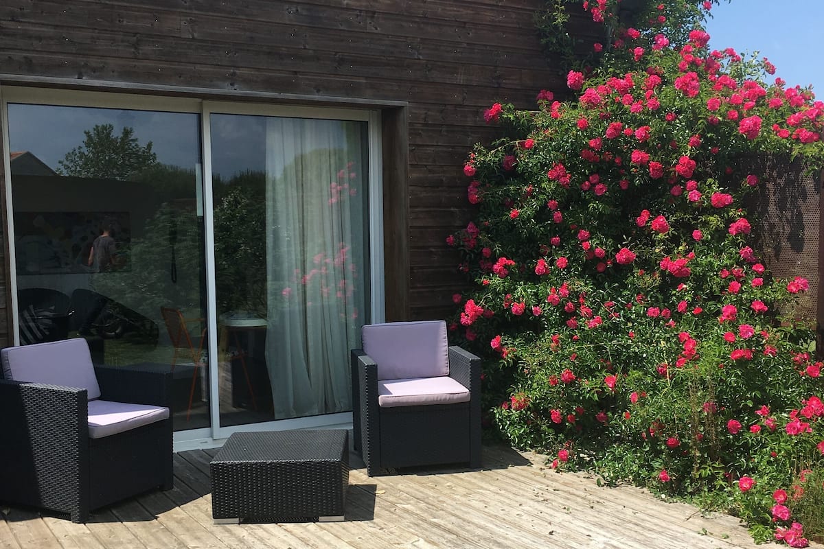 A patio with two wicker chairs, a wooden deck, and a large window with a view of the sky.