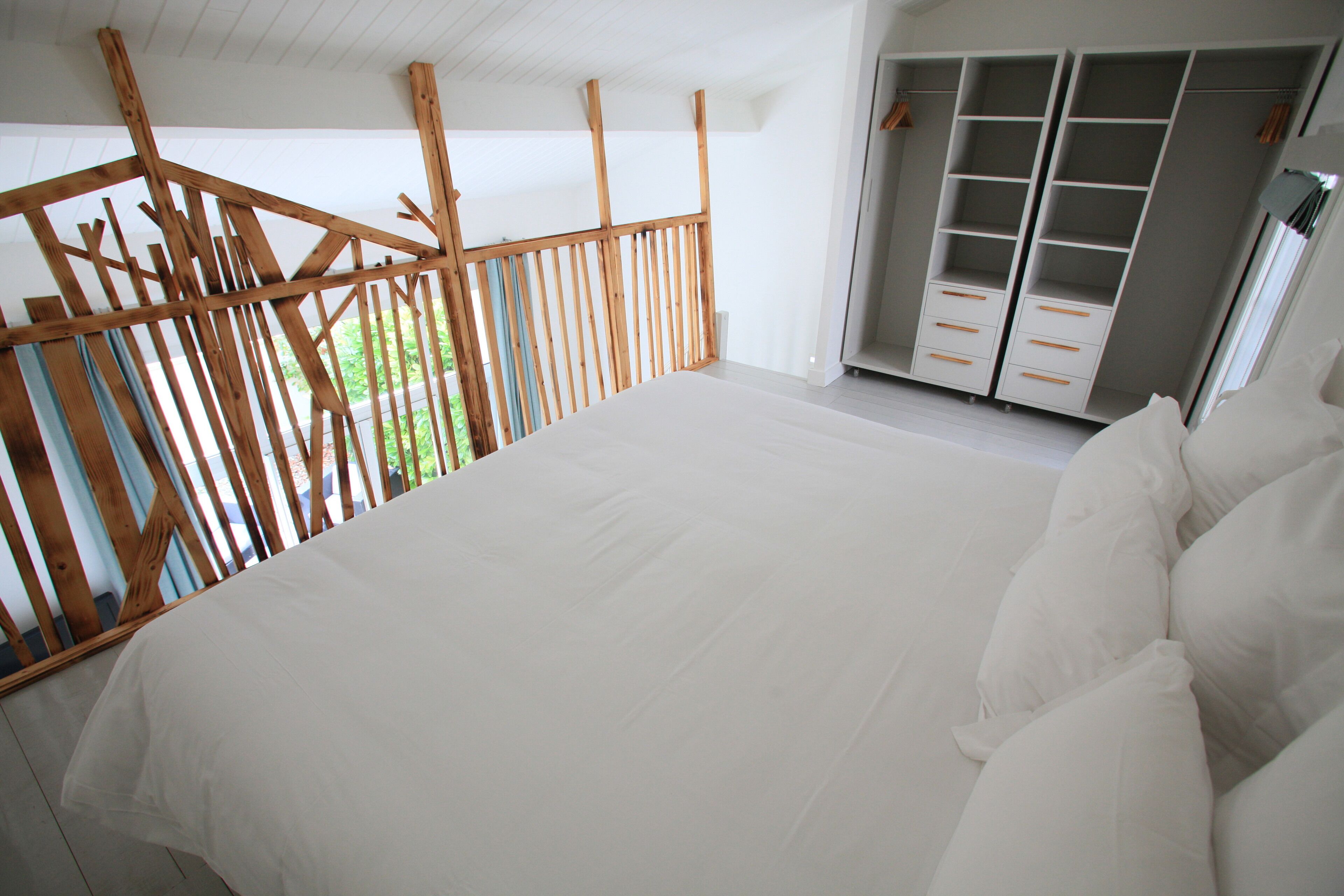 A bedroom with a large bed, wooden balcony railing, and a walk-in closet.