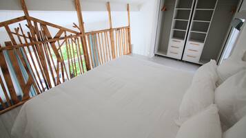 A bedroom with a large bed, wooden balcony railing, and a walk-in closet.