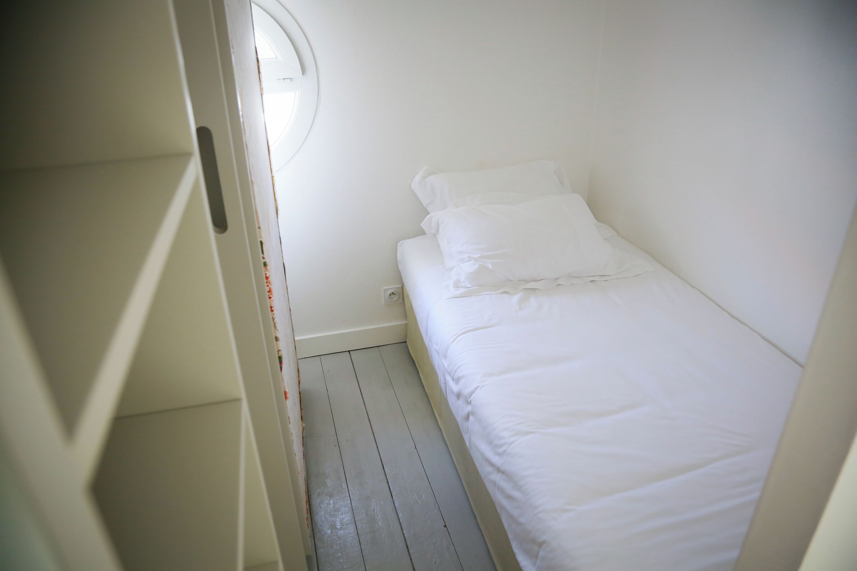 Una piccola camera da letto con un letto singolo, pavimenti in legno e una finestra sul lato sinistro.