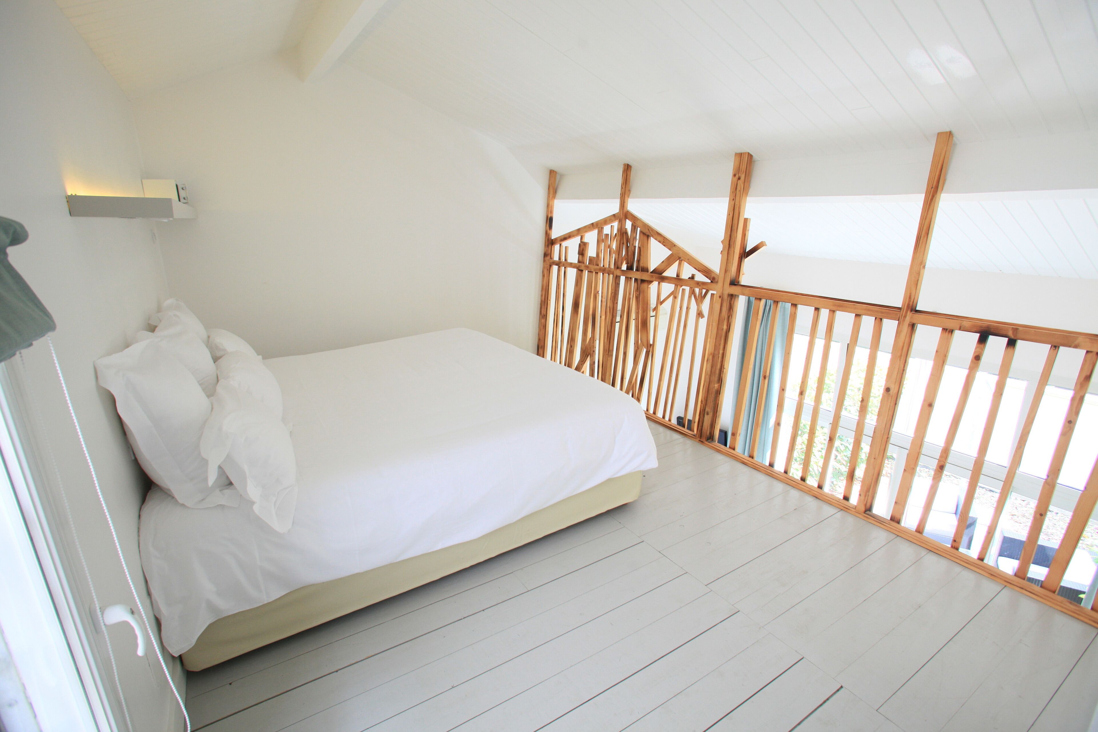 A bedroom with a bed, white walls, and a wooden railing.