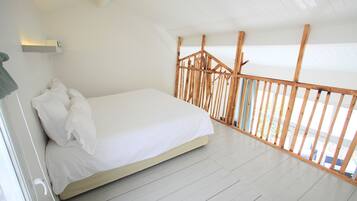 A bedroom with a bed, white walls, and a wooden railing.