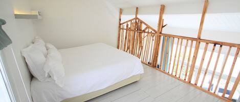 A bedroom with a bed, white walls, and a wooden railing.