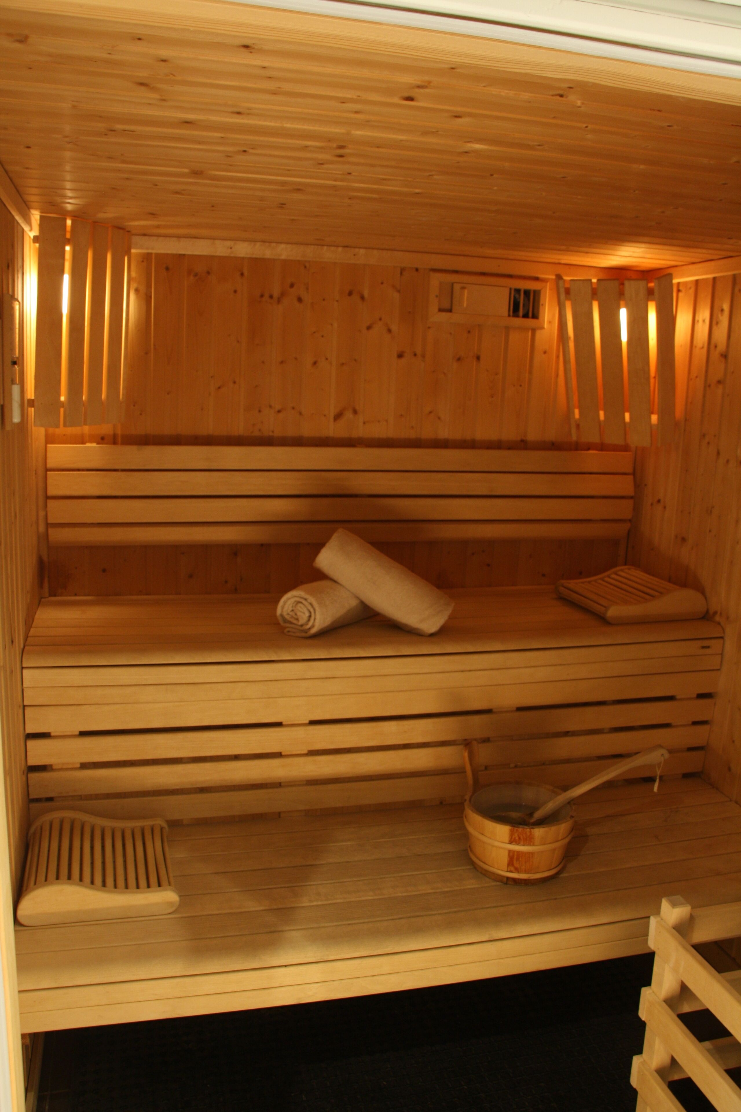 Uma sauna de madeira com bancos, um assento e um apoio para os pés, além de um balde de madeira.