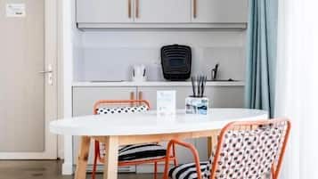 A dining area with a white table and two patterned chairs, a kitchen in the background, and a door to the left.