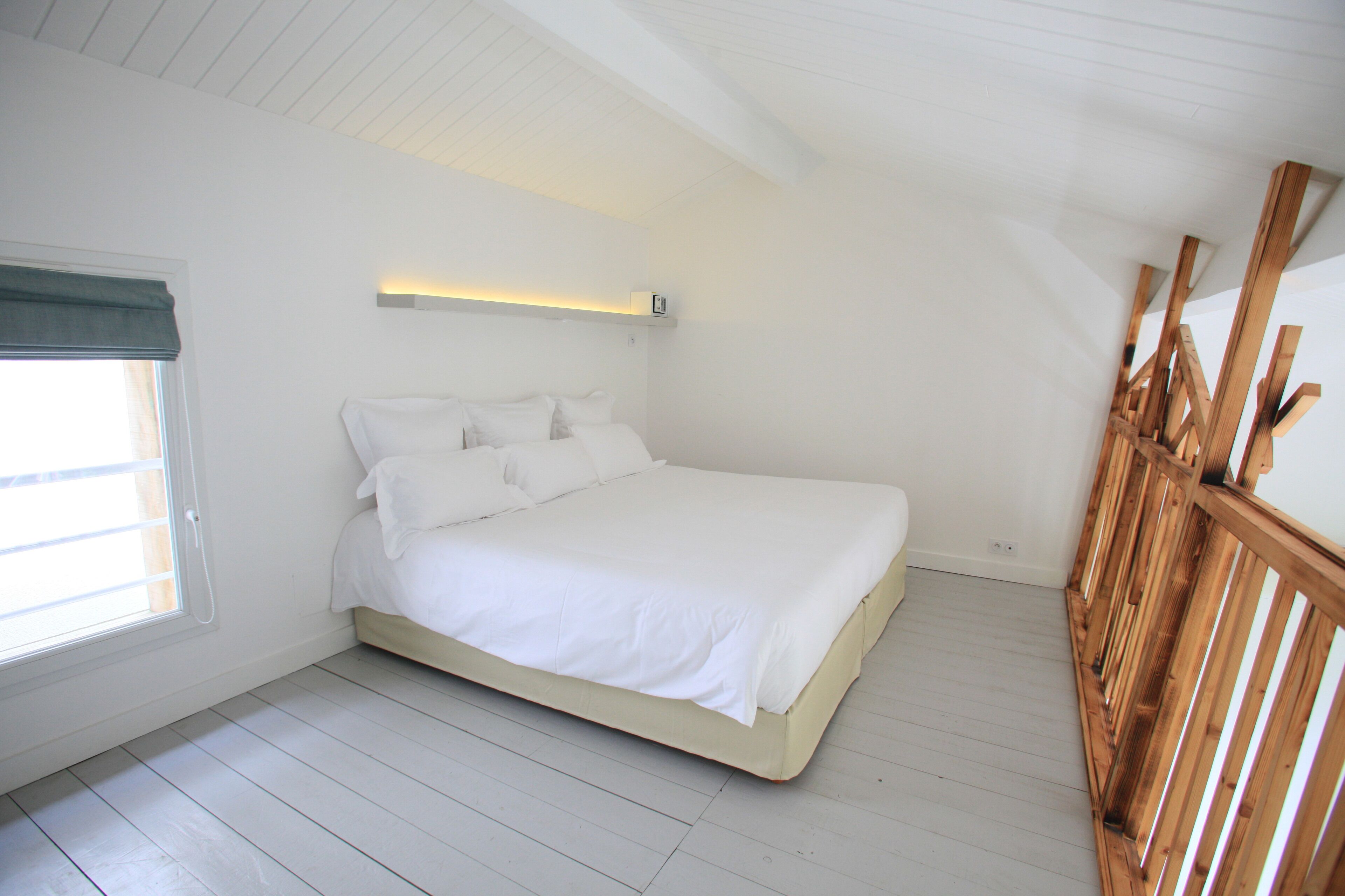 A bedroom with a bed, a window with a curtain, and a wooden railing.
