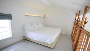 A bedroom with a bed, a window with a curtain, and a wooden railing.