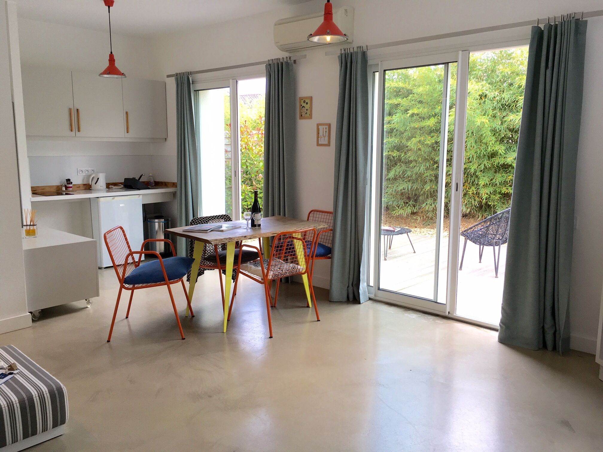 A modern kitchen with a dining area, large sliding glass doors to a garden, and a small refrigerator.