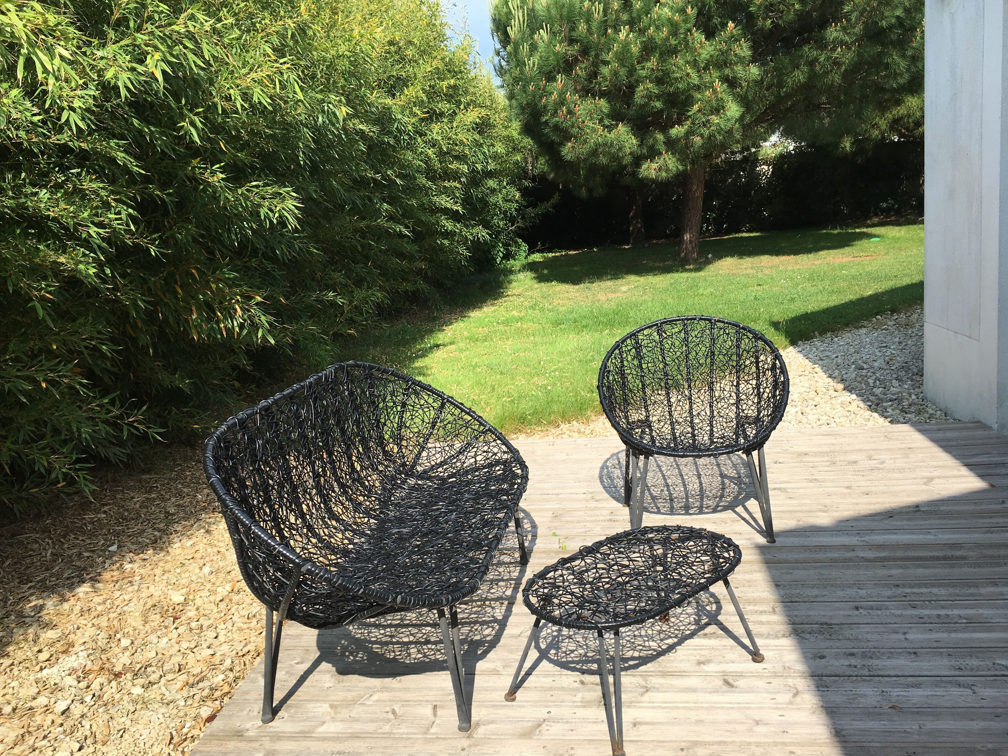 Two outdoor wicker chairs on a wooden deck with a grassy lawn and trees in the background.