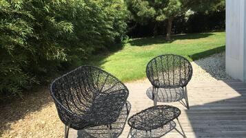 Two outdoor wicker chairs on a wooden deck with a grassy lawn and trees in the background.