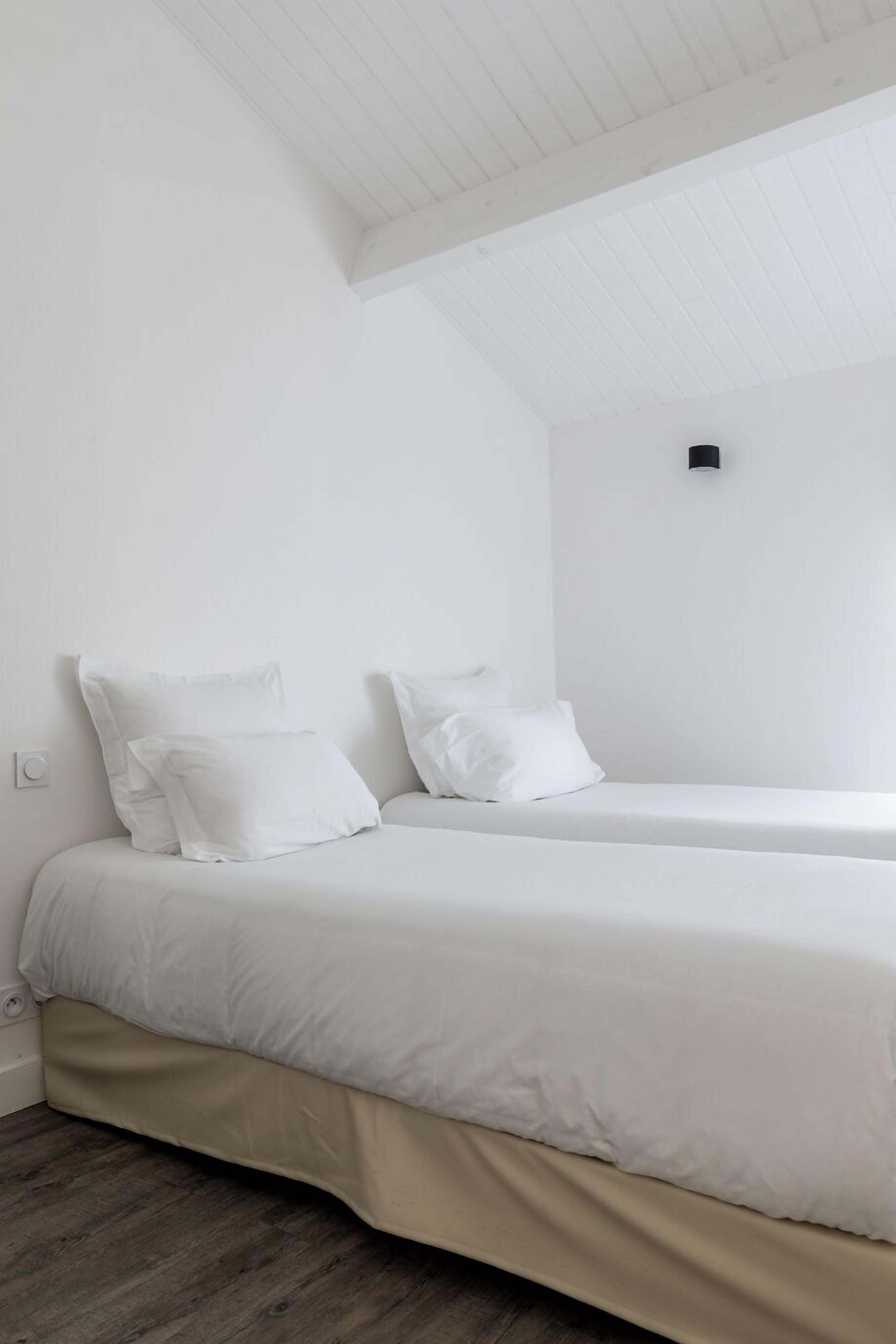 A minimalist room with a bed, two pillows, and a light switch on the wall.