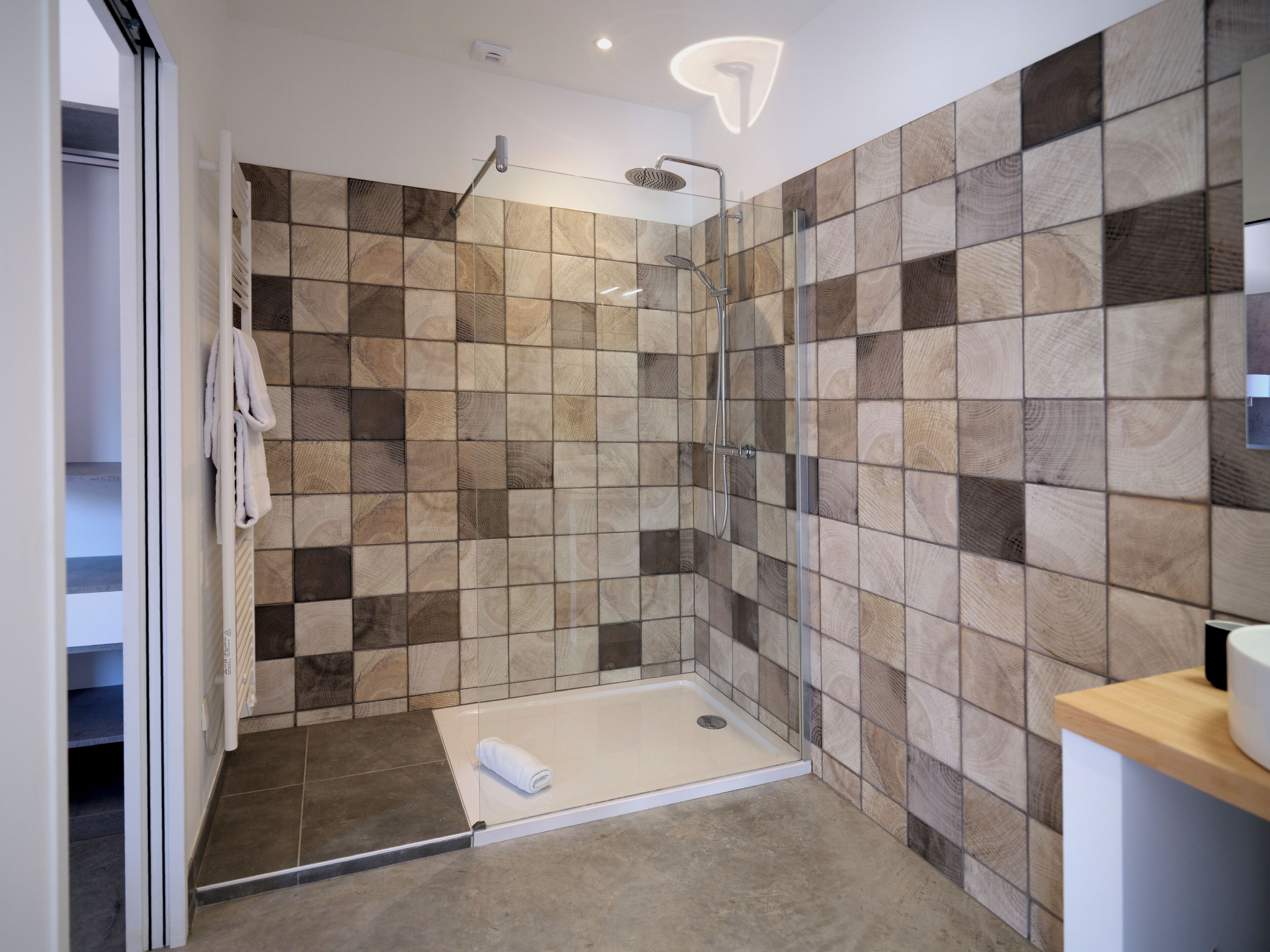 Un área de ducha moderna con puerta de vidrio, pared con azulejos de madera y un lavamanos blanco con encimera de madera.