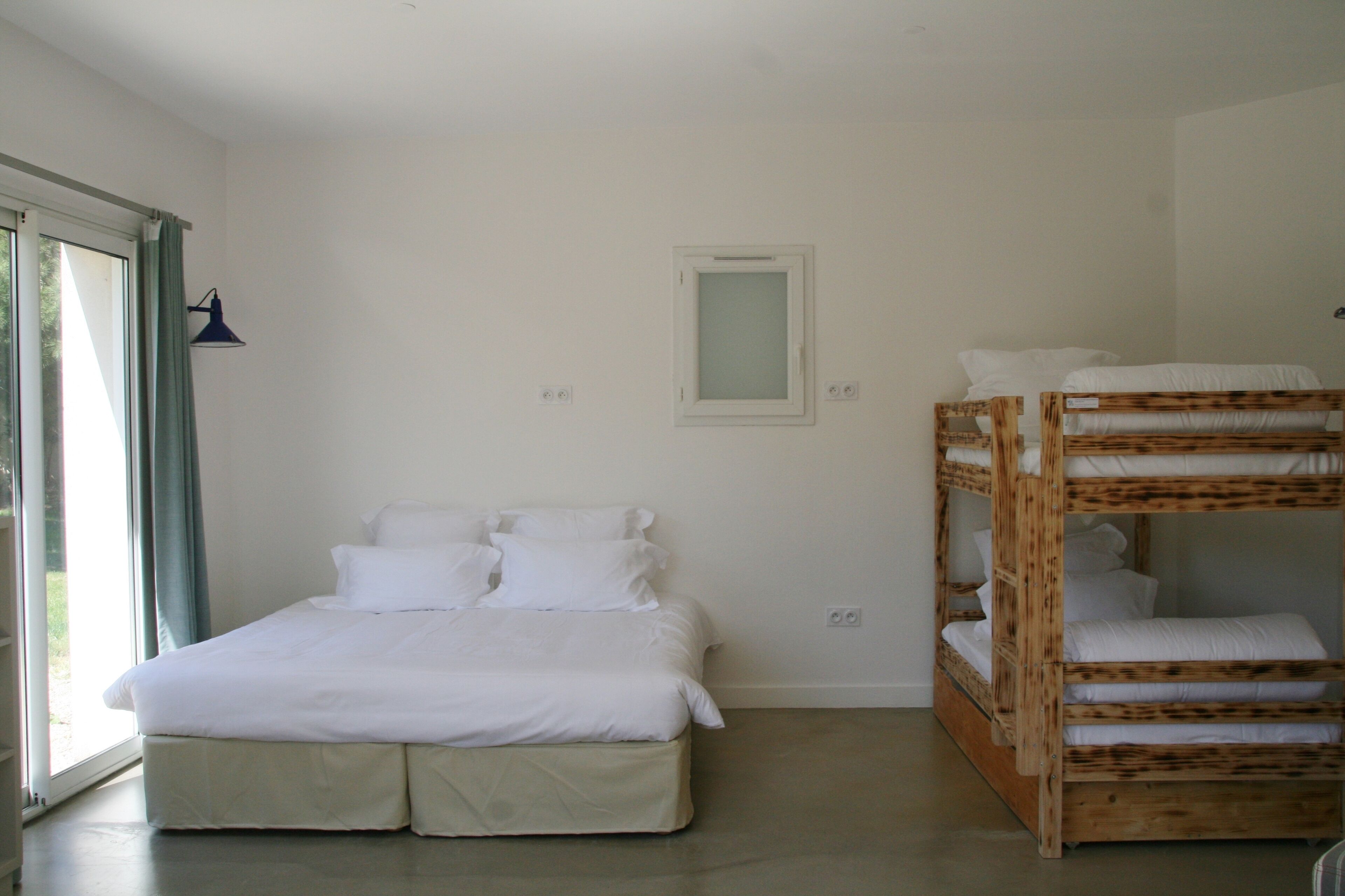 Un dormitorio con cama individual, literas, una ventana con cortinas y un aplique de pared.