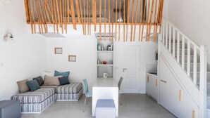 A modern, open-plan living space with a sofa, dining table, and staircase. - Côté Océan (Angoulins)
