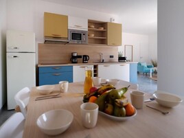 Una cocina moderna con microondas, cafetera y armarios de madera. Hay una mesa de comedor con tazones y un frutero.
