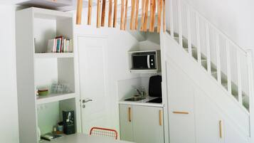 A modern kitchen with white cabinetry, a dining table, and orange chairs. A staircase with wooden railings leads to an upper level.