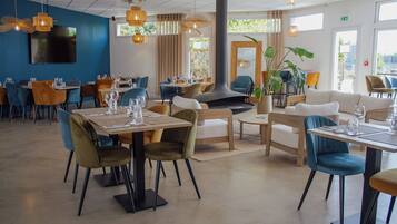 A modern restaurant with multiple dining areas, including a central seating area with a fireplace, surrounded by tables and chairs.