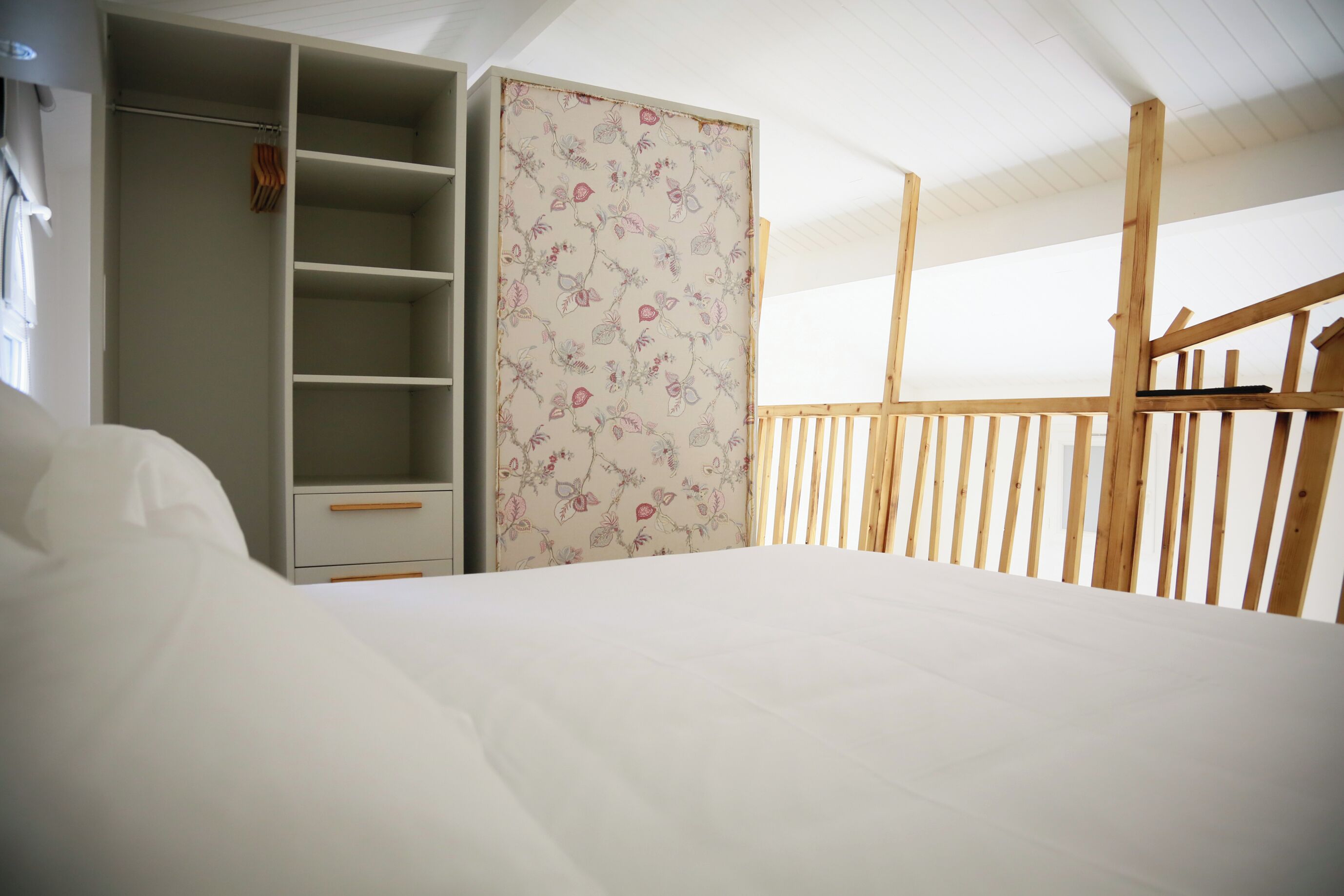 A bedroom with a bed, a wardrobe, and a balcony with wooden railings.