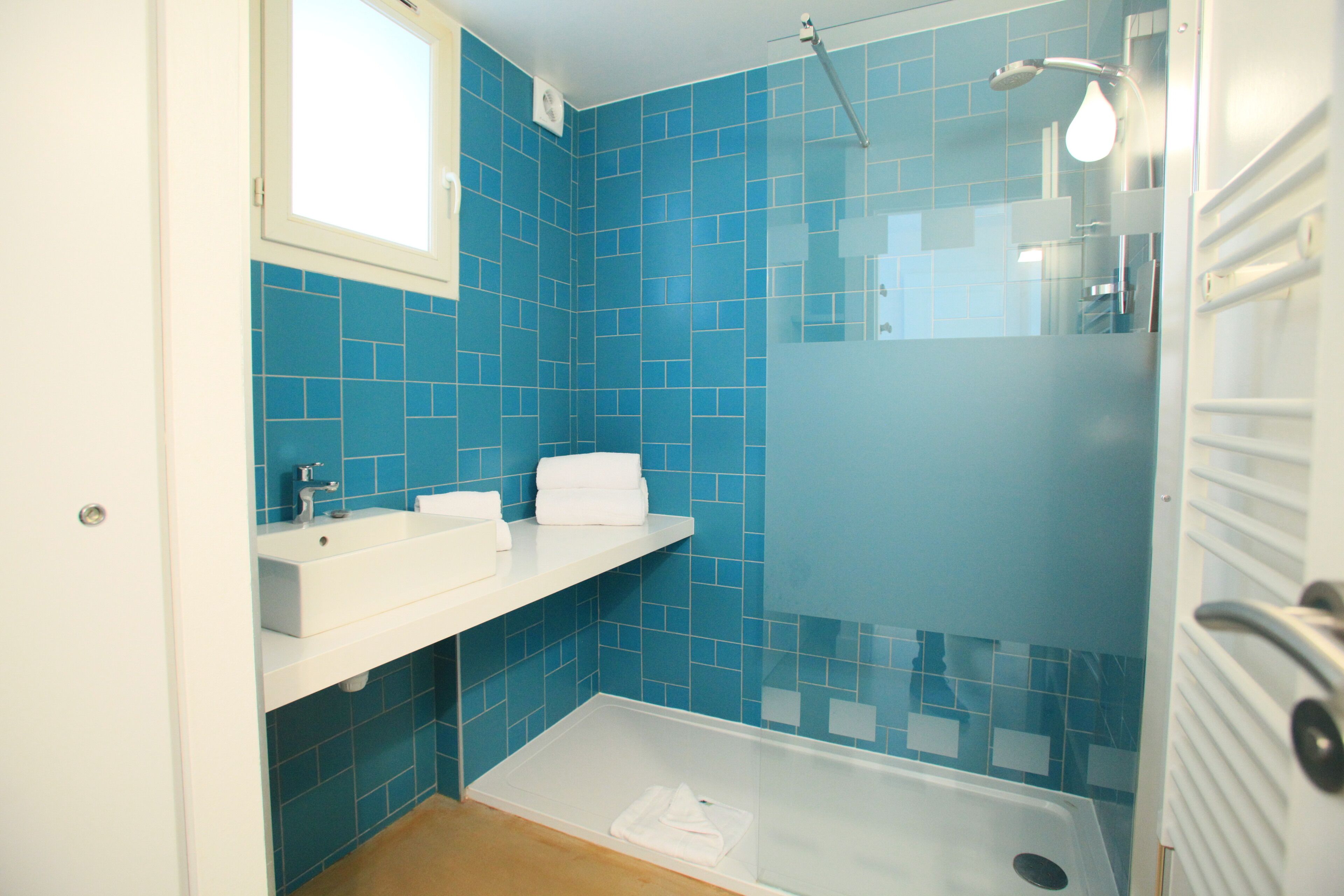 Un baño con azulejos azules, un lavamanos blanco, un espejo y una ducha.