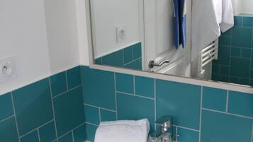 A bathroom with a white sink, blue tiles, a mirror, and a towel rack with a hat.