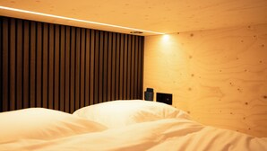 Een slaapkamer met een houten hoofdbord, een bed met witte lakens en een nachtkastje dat aan de muur is bevestigd.