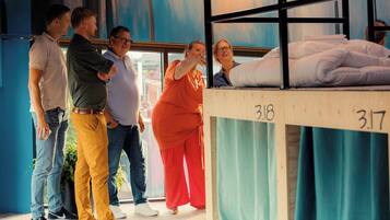 Cama litera con los números 318 y 317, un grupo de personas de pie, y una ventana con vistas.