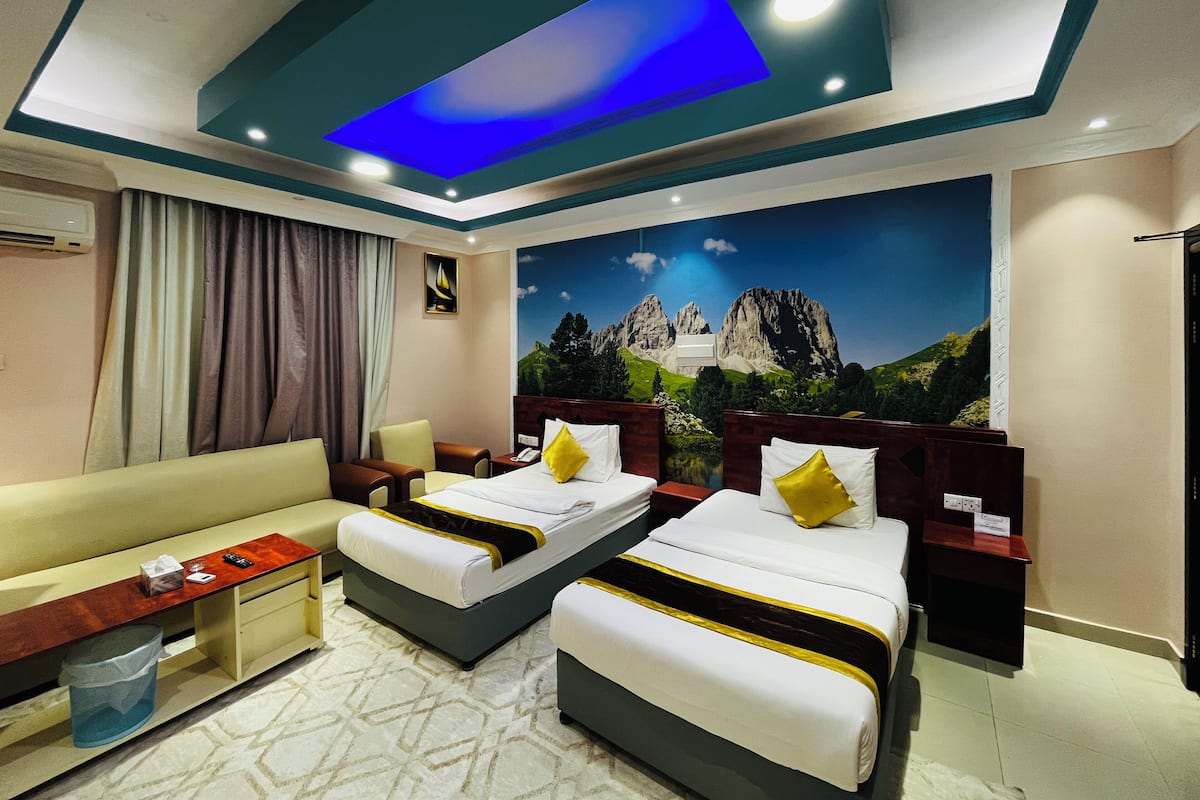 Ein Hotelzimmer mit zwei Betten, einer Sitzecke, einem Schreibtisch und einem großen Wandbild von Bergen.