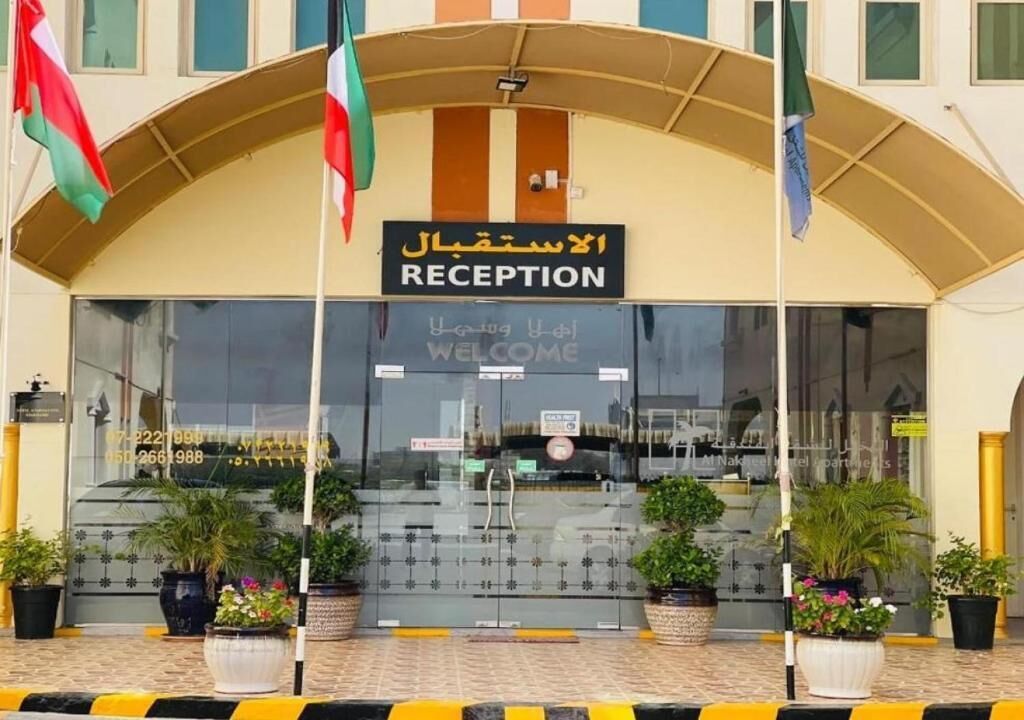 Una recepción de hotel con un cartel en árabe e inglés, un letrero de bienvenida y plantas en macetas al frente.