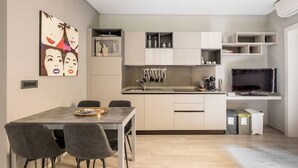 A modern kitchen with white cabinets, a dining table with chairs, and a flat-screen TV. - Mandria Apartments 2 (Bologna)