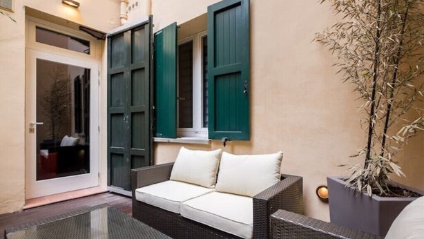 A cozy outdoor seating area with a wicker sofa, a glass table, and a potted plant. - Mandria Apartments 2 (Bologna)
