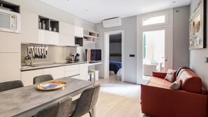 A modern kitchen with white cabinets, a dining table with chairs, and a red sofa in the living area. - Mandria Apartments 2 (Bologna)
