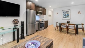 A modern kitchen with stainless steel appliances, a dining area with a glass table, and a flat-screen TV mounted on the wall. - The Sweetest Hideaway - 81 Walkscore! (Seattle)