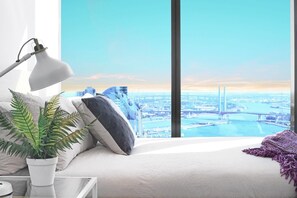 A modern bedroom with a large window overlooking a cityscape, including a bridge and skyscrapers.