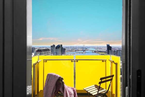 A balcony with yellow railings, a wooden bench, and a towel draped over a chair.