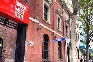A red brick building with a sign reading "Upper West Side" and a blue street sign for "Watertank Way."