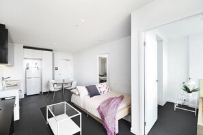 Une chambre d’hôtel moderne et minimaliste, comprenant un lit, un petit bureau, une chaise, une table basse en verre et un téléviseur.