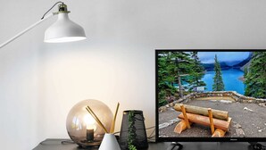 Un bureau sur lequel se trouve un écran d’ordinateur affichant une vue panoramique sur un lac, une lampe de bureau, un objet sphérique en verre et une petite plante.