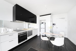 Une cuisine moderne dotée d’un grand téléviseur à écran plat, d’un four encastré et d’un coin repas avec une table en verre et des chaises blanches.