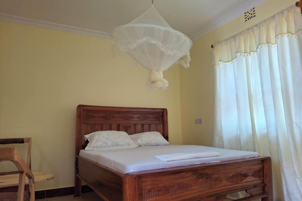 A wooden bed with a canopy, a chair, and a window with curtains.