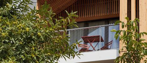 Een modern gebouw met een houten gevel, een balkon met rode meubels, en een boom op de voorgrond.