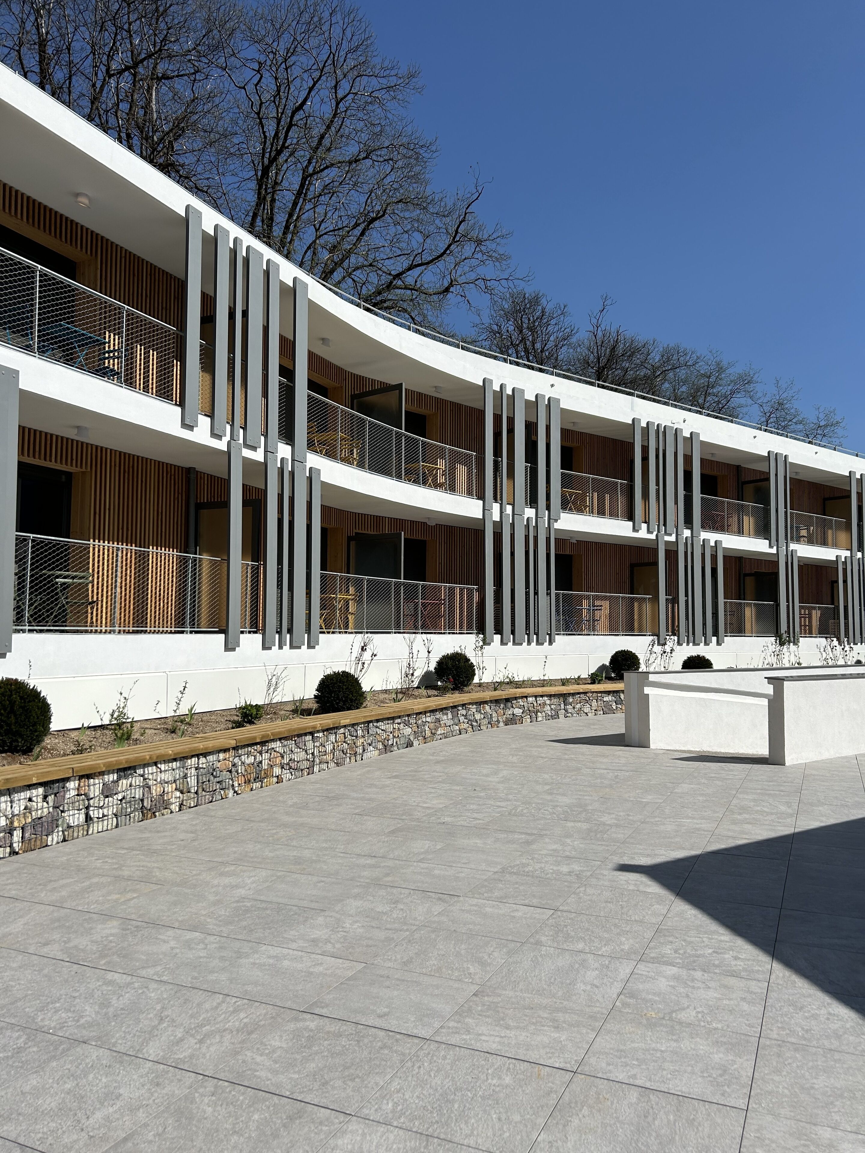 A modern multi-story building with balconies, a stone pathway, and a clear sky.