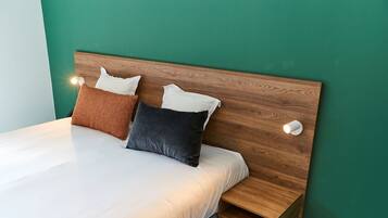 Una cama bien hecha con sábanas blancas y dos almohadas, un cabecero de madera y una mesita de noche con una lámpara.
