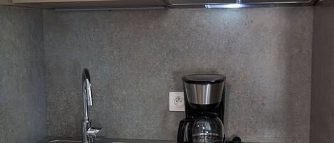 A compact kitchen with a microwave, coffee maker, and a sink.