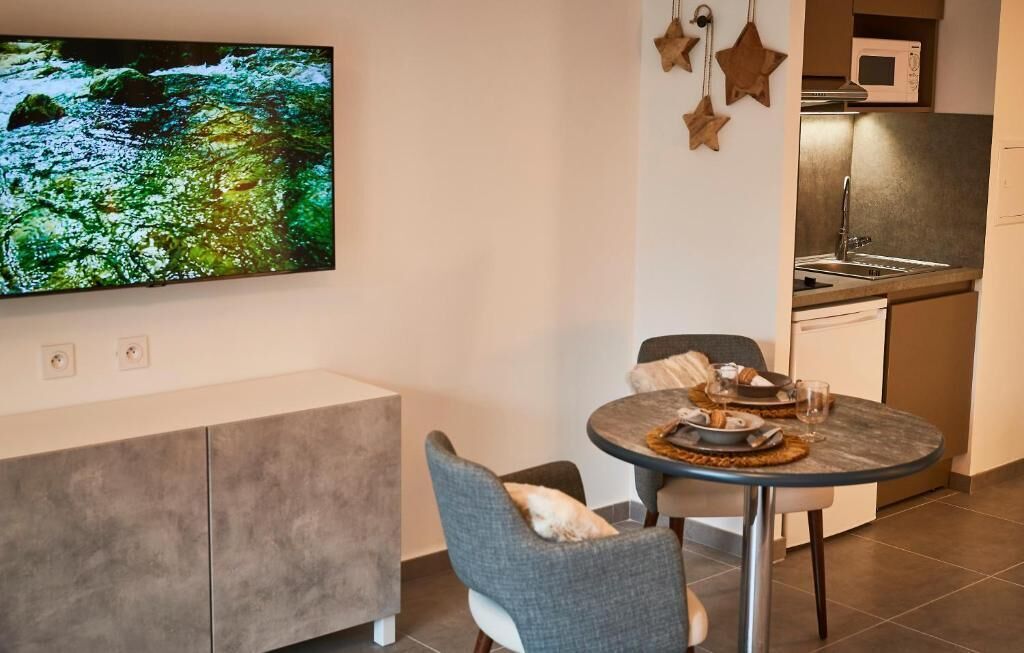 Une cuisine moderne équipée d’un four à micro-ondes, d’un évier et de placards. On y trouve également un coin repas avec une table et des chaises, ainsi qu’un téléviseur à écran plat fixé au mur.