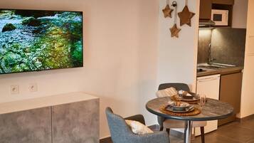 Une cuisine moderne équipée d’un four à micro-ondes, d’un évier et de placards. On y trouve également un coin repas avec une table et des chaises, ainsi qu’un téléviseur à écran plat fixé au mur.
