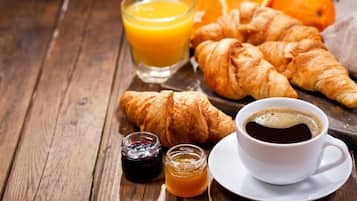 Een ontbijt met croissants, sinaasappelsap, koffie en jam op een houten tafel.